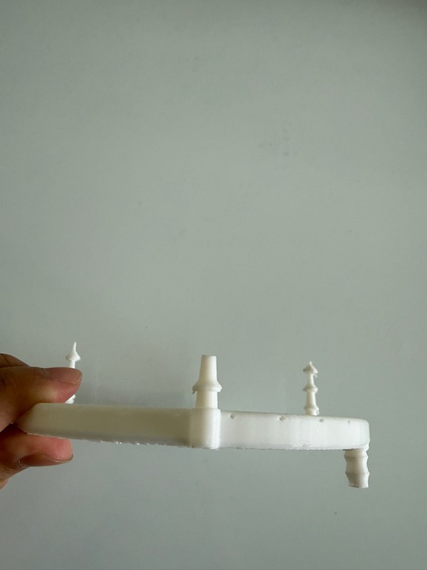 A flat white printed bar held in one hand against a wall, with barbed outlets standing up along its length.
