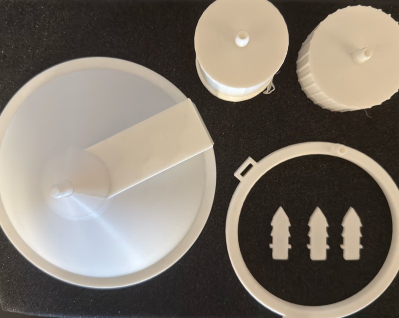 The drip kit laid out on black foam: a cone-shaped root cap, the two parts of the flow controller, the drip ring, and three stakes.